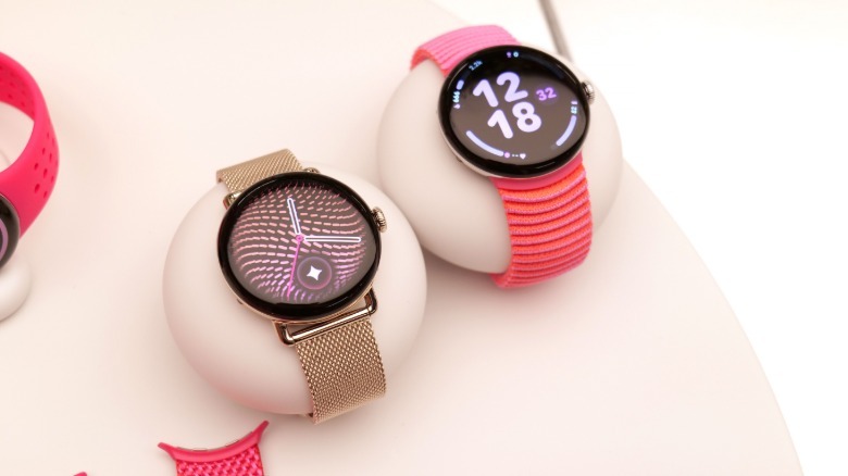 A pair of Pixel Watch 5 units on display. One has a metallic mesh band while the other has a pink woven loop strap.