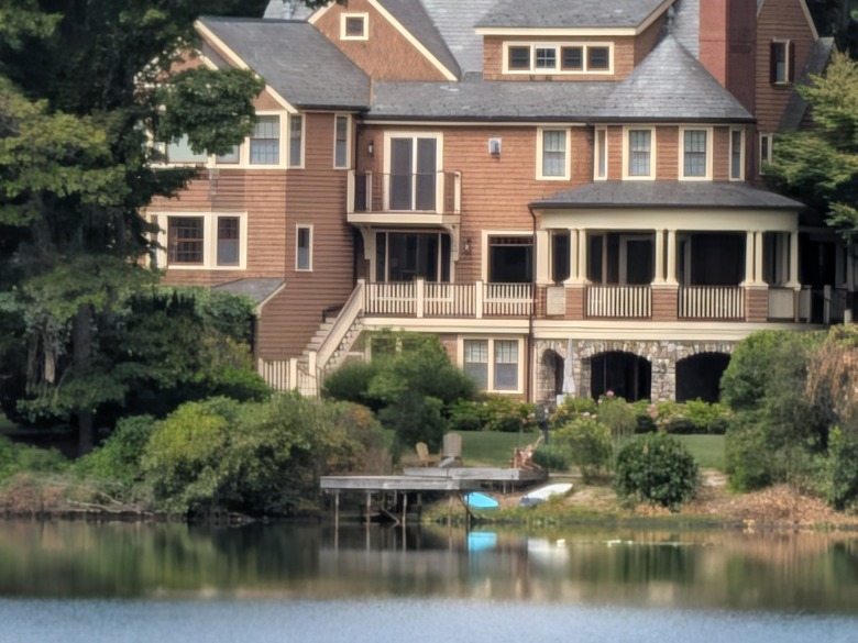 A peach-colored house with many roofs in front of a lake.