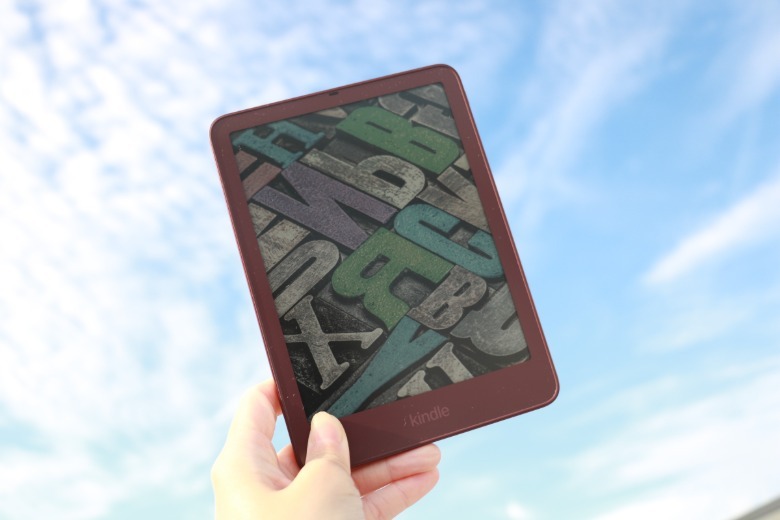A fig Kindle Colorsoft Signature Edition held up against a blue sky.